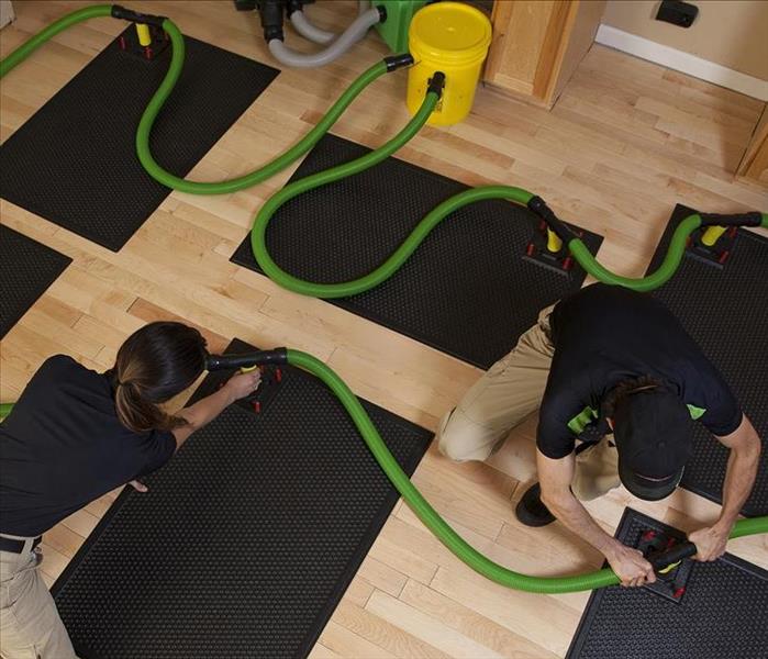SERVPRO technicians installing Injectidry water removal system on hardwood floor